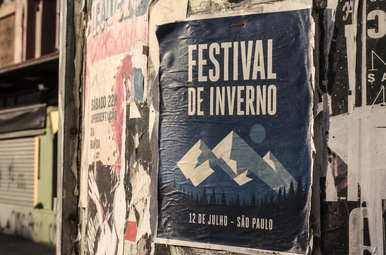 Cartaz de festival impresso em serigrafia, colado num muro de lambe-lambe, com o texto legível
